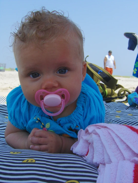 a baby on the beach wearing a pacifier