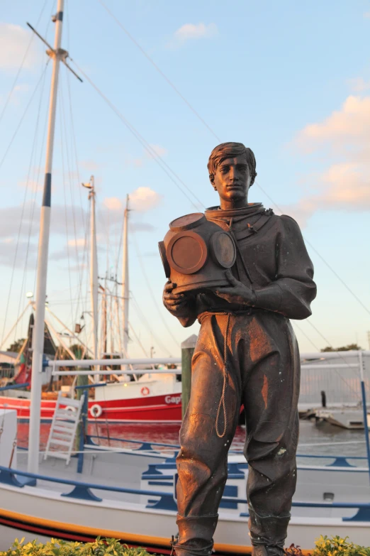 statue of man in an overalls and diving mask standing next to a large boat