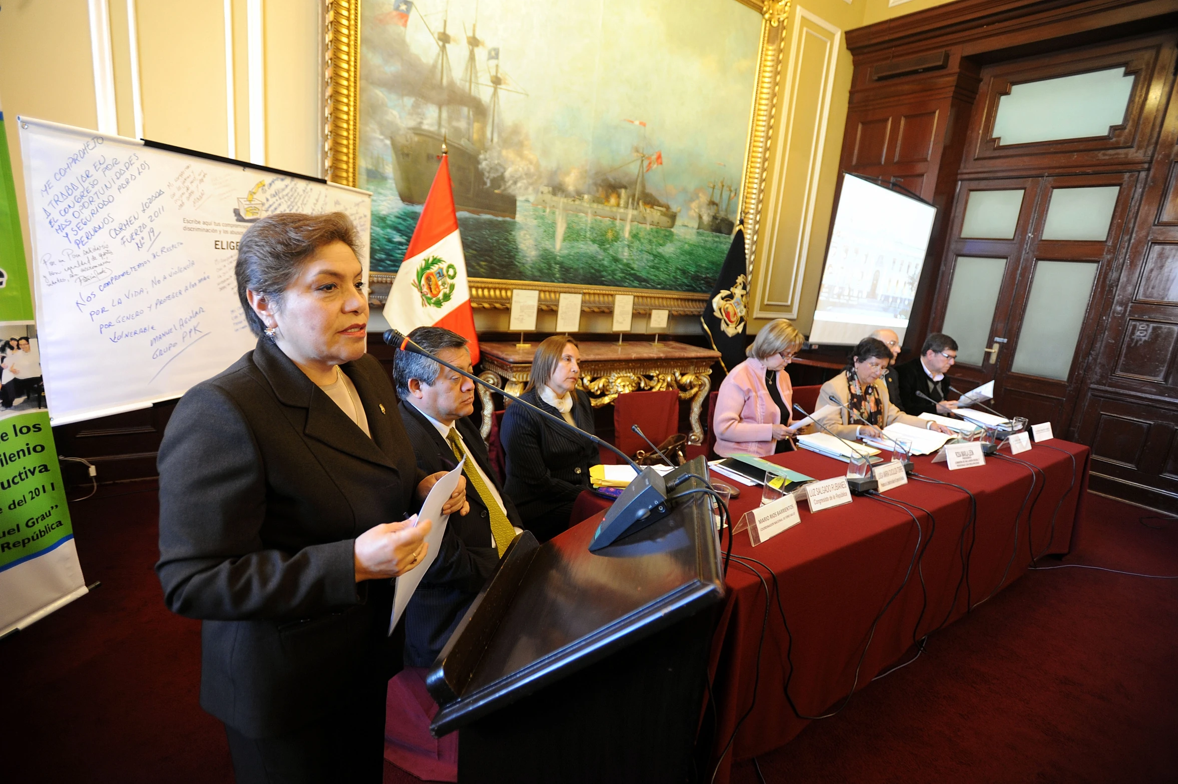 a woman speaking into a microphone with people sitting at the back