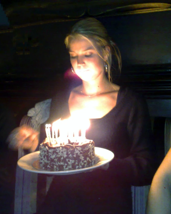 woman holding up cake with lit candles in front of her