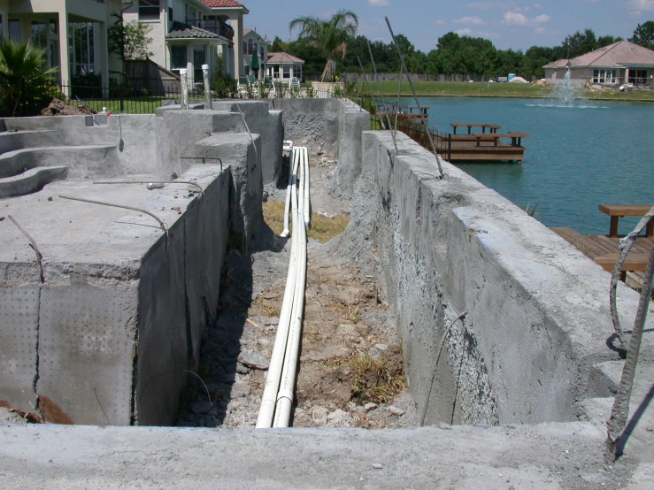 a cement wall with an exposed drain next to a body of water