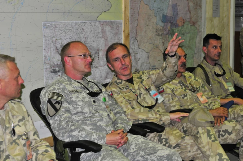 military soldiers sitting in chairs while one gestures up