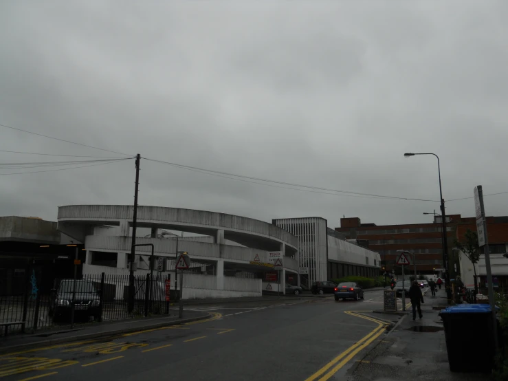 a man walks in the rain near an intersection with a parking lot and bus stop