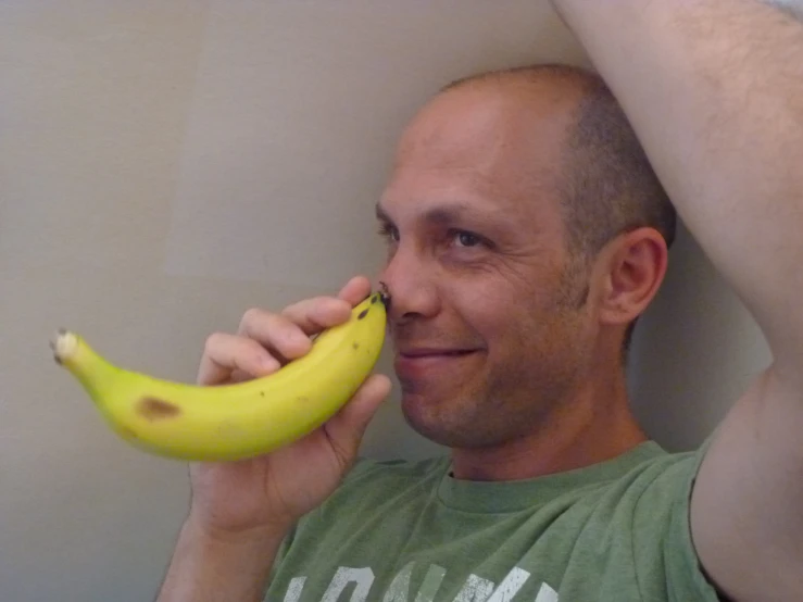 a man leaning against a wall, holding a banana