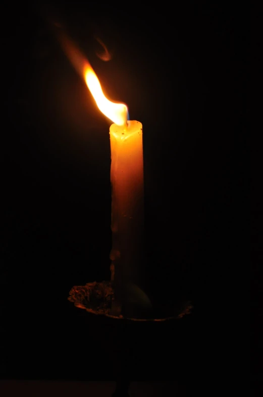 a candle with an orange flame burning in the dark