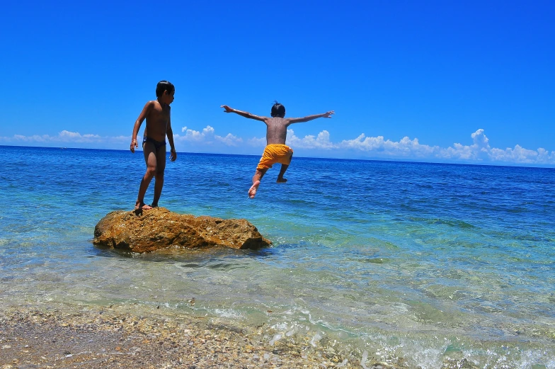 two men jumping off rocks into the ocean