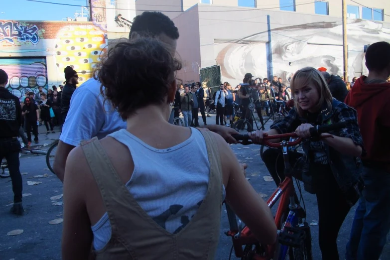 people crowd together standing near a street with bicycles