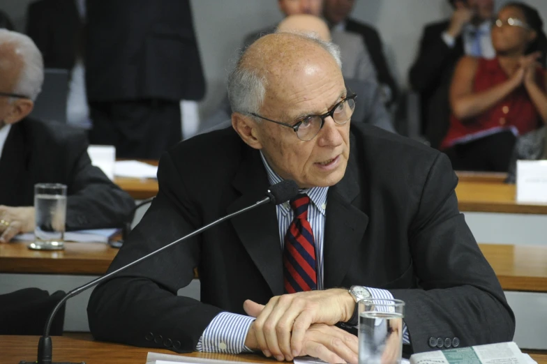 a man sitting at a desk next to microphones in front of people