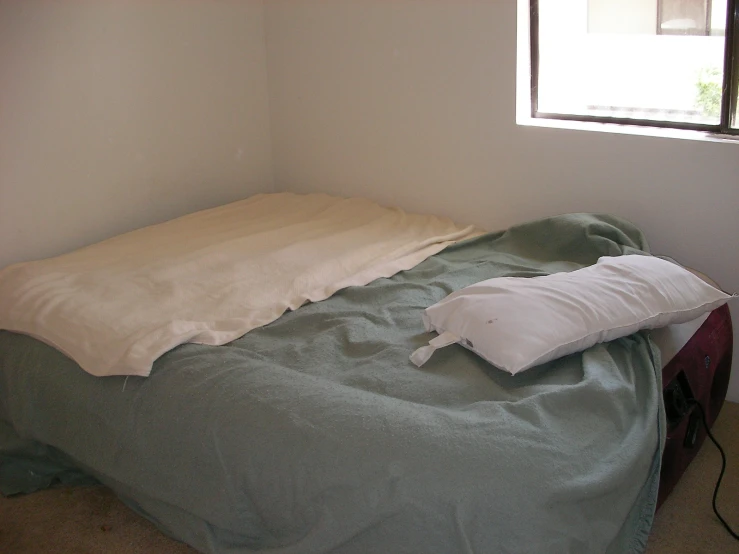 a bed with an unmade comforter next to a window