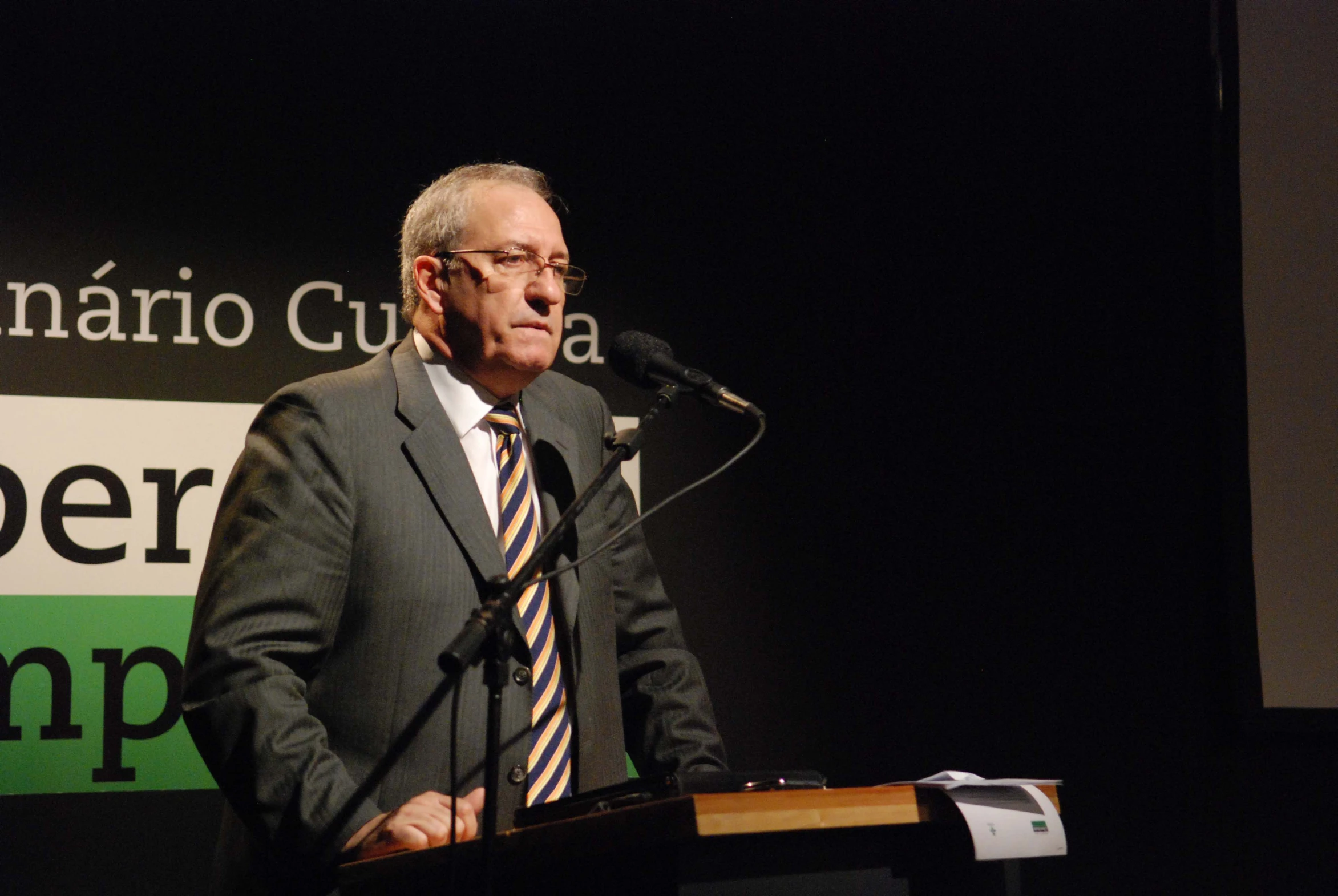 a man wearing glasses is at a podium with a microphone