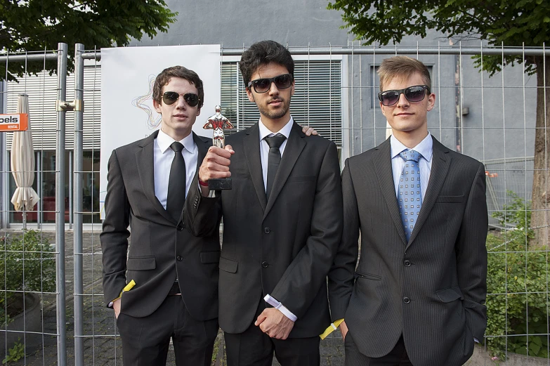 three young men dressed in suits and sunglasses standing in front of a fence