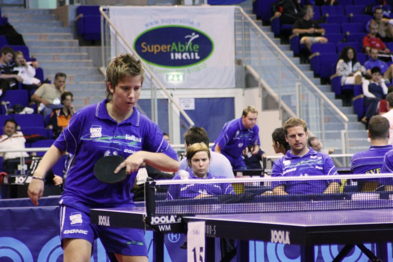 some people in blue shirts standing around playing ping pong