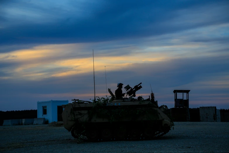 a large tank parked on a gravel road next to an old building