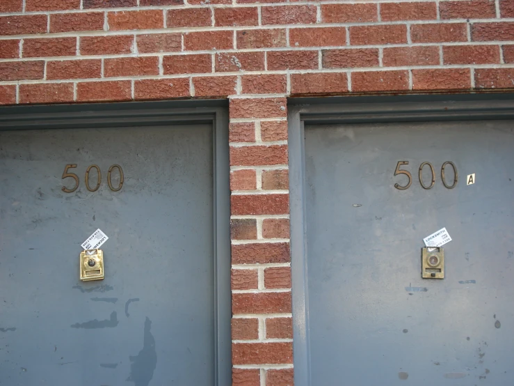 two blue doors with white numbers in front of a brick wall