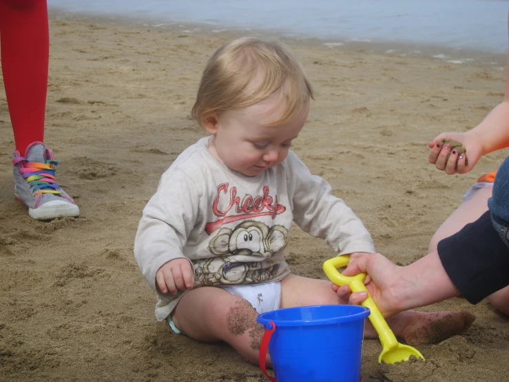 a baby playing in the sand with a bucket