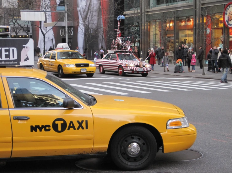 taxi cabs and people crossing the street in front of a building