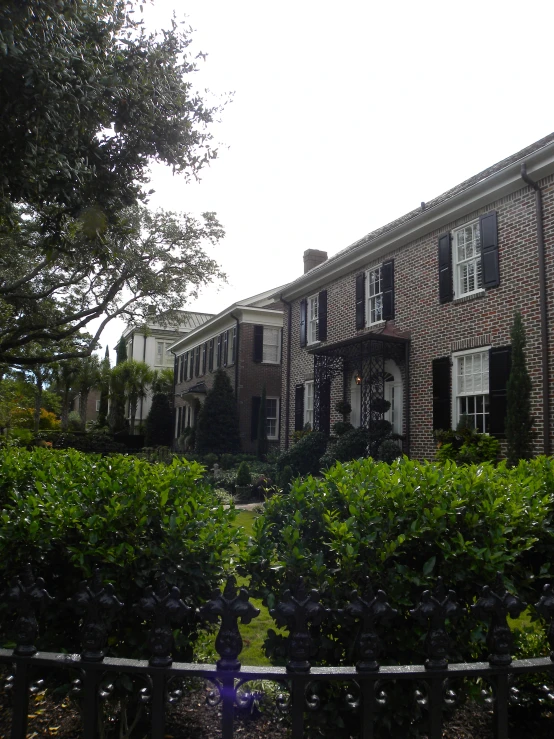 a house with many trees and bushes behind the fence