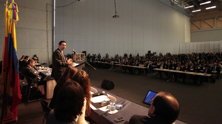 a man speaking to a group in front of a large group of people