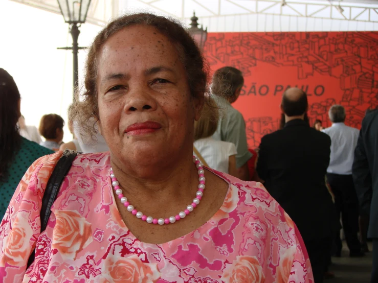 a woman wearing a pearl necklace in front of a red wall