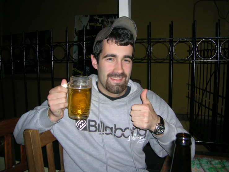 a man holds up two beers while sitting at a table