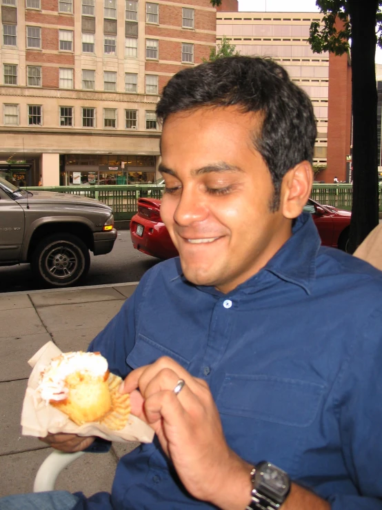 a man smiling and eating a sandwich on the sidewalk