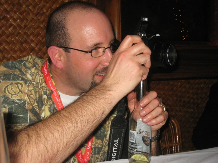 a man holding a camera up to his face with a bottle in front of him