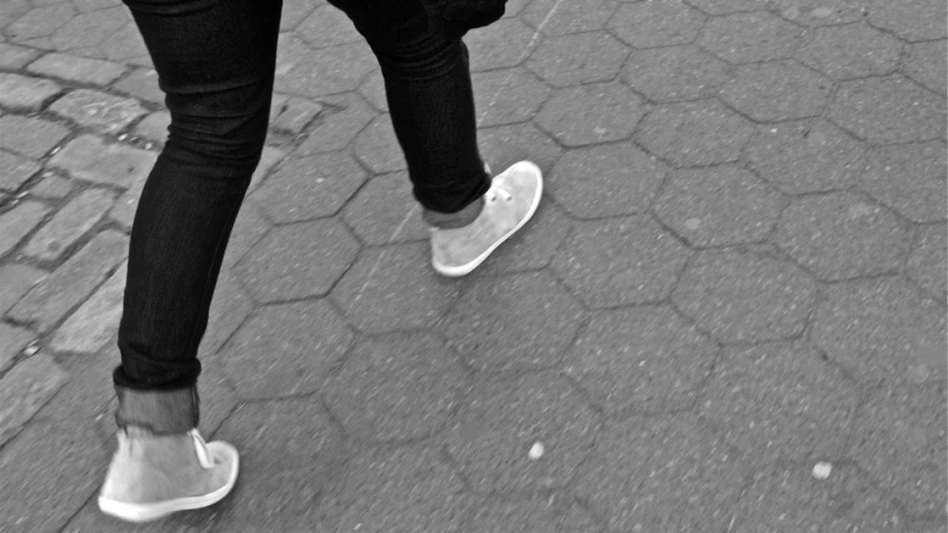 a woman's legs in white tennis shoes walking along a brick path