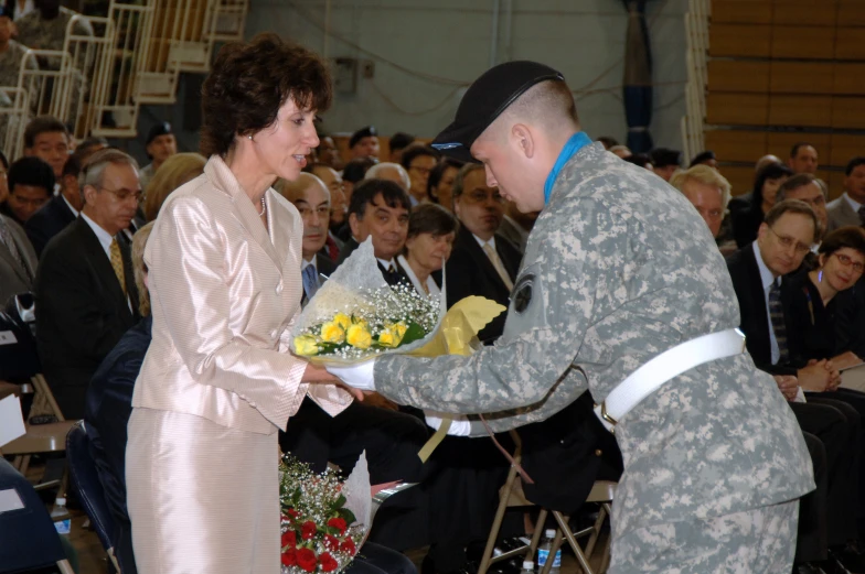 a military soldier presents flowers to a woman