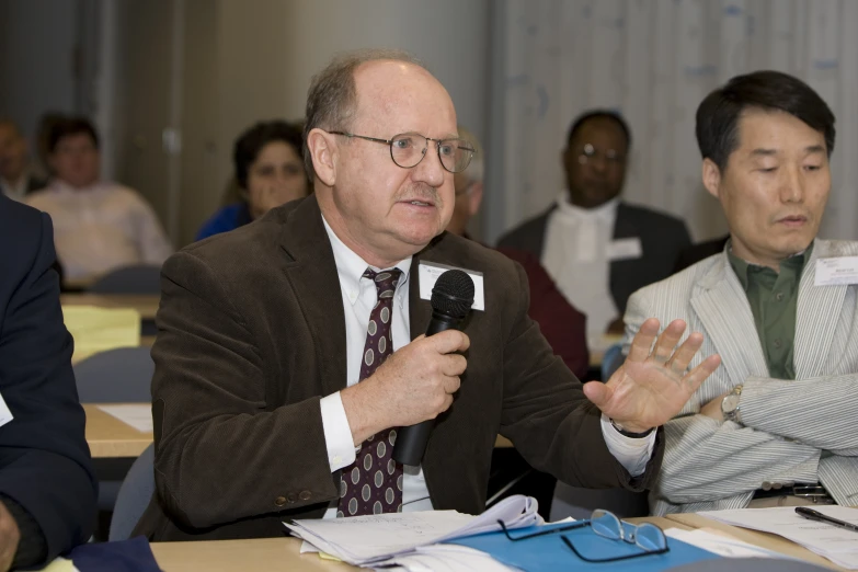 a man in business attire holds up a remote control to speak to a group