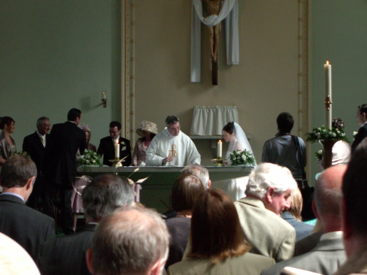 a priest sits at a pew, speaking to the crowd