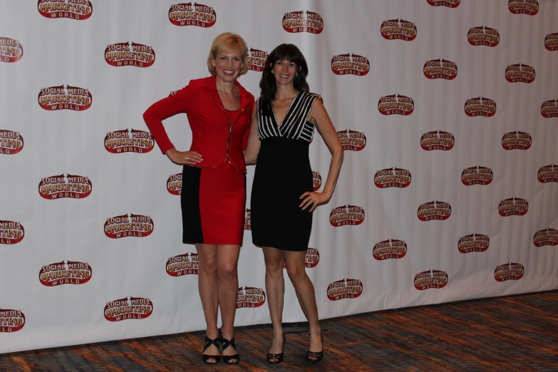 two woman stand near one another in front of a wall