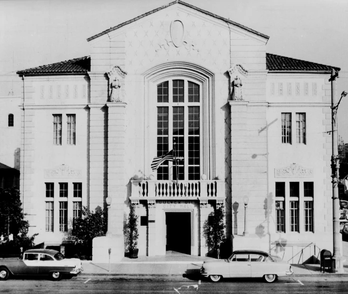 a black and white pograph shows cars driving past an ornate building