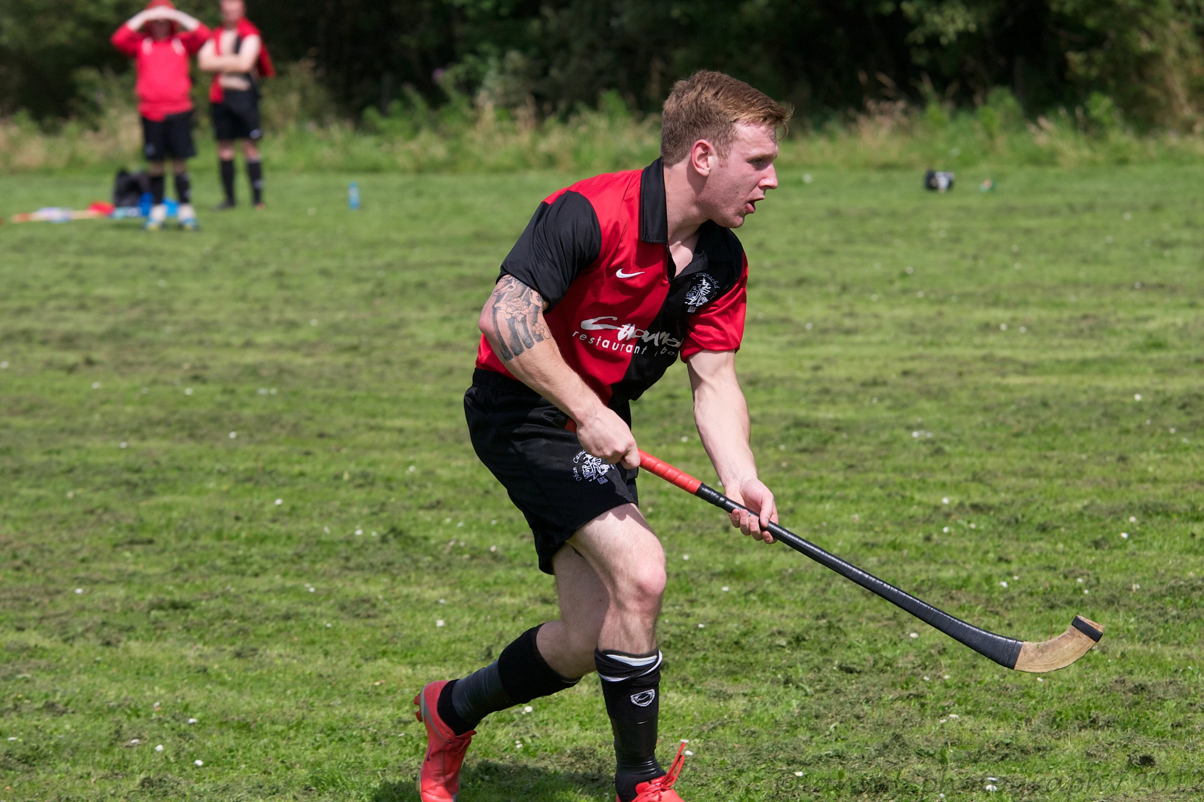 a man in red jersey with hockey stick in grassy field