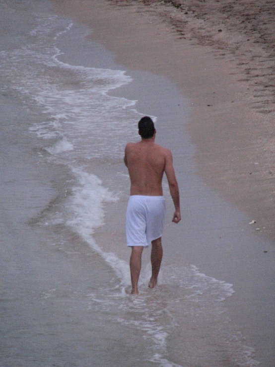 a man in white shorts walking on beach