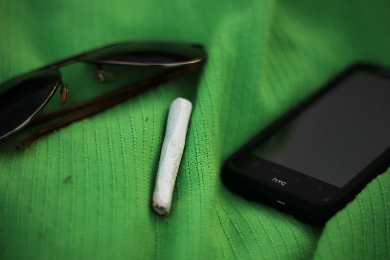 some glasses some cellphone and a cigarette on a green cloth