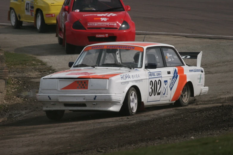 a car with an orange stripe on it races behind a red car