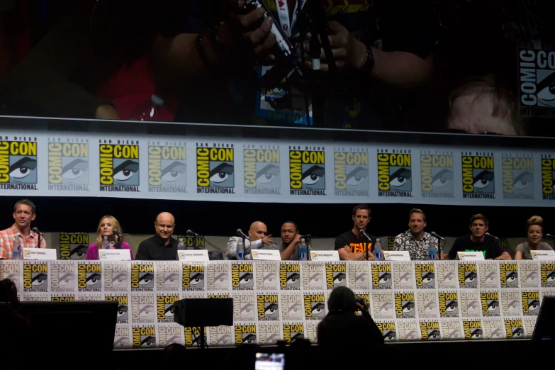 many actors are sitting behind a small table at a convention