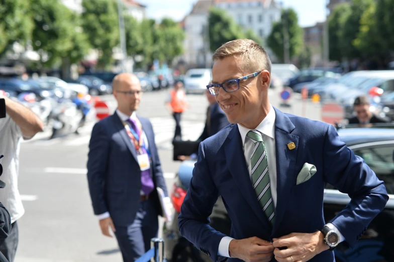 a man in suit and tie standing on a street with cars