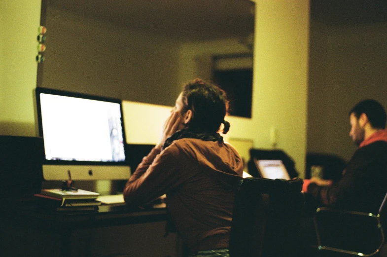 two people sit at computers in a dimly lit room