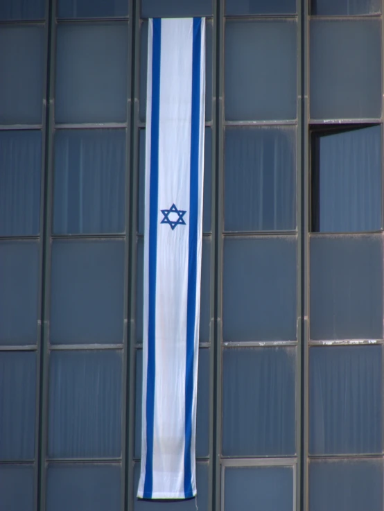 an israeli flag in the shape of the letter h hanging on a building