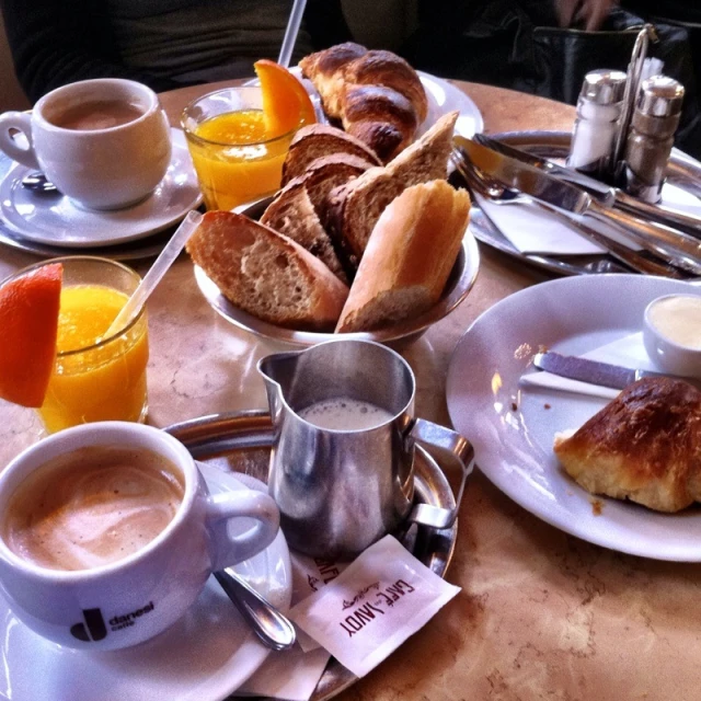 a table with breakfast food on it and bread, muffins, juice, glasses of orange juice