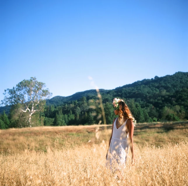 a woman walking through a field in front of a mountain