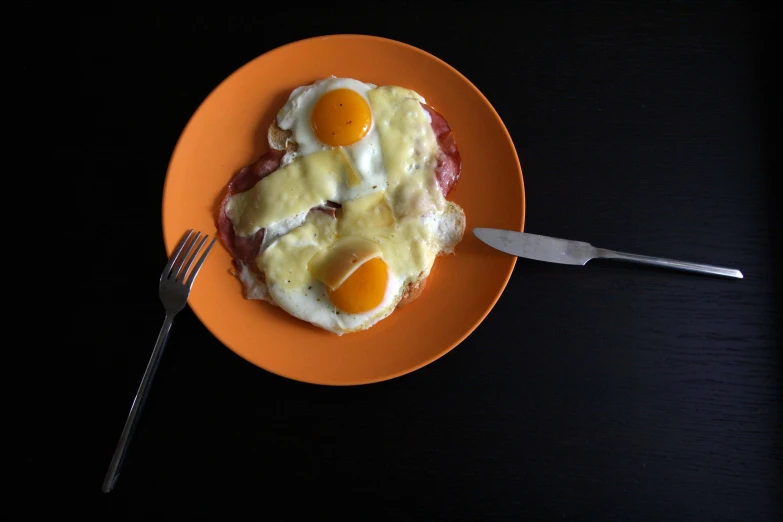 a close up of an orange plate of food with eggs and ham