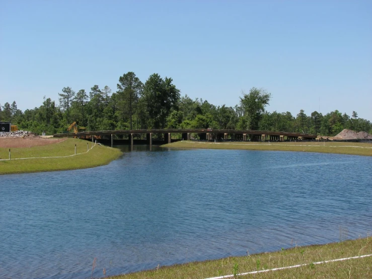 a lake near some trees and grass under a bridge