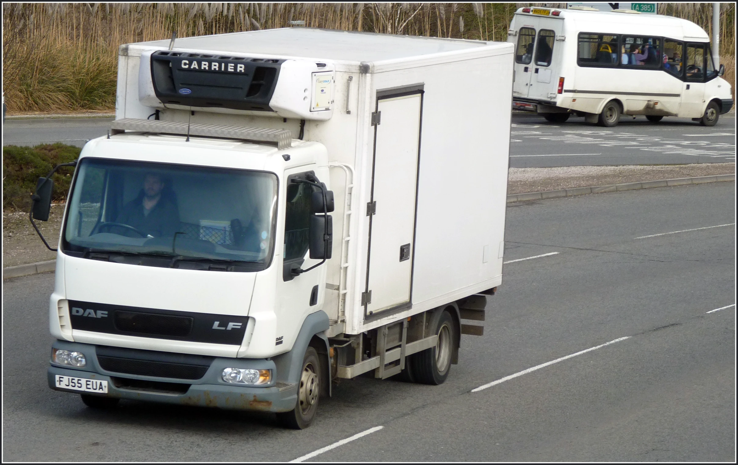 a white truck driving down a road past a bunch of trucks