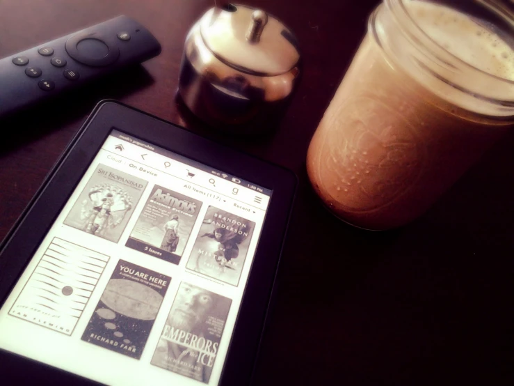 a tablet with a news paper on it next to a glass of brown liquid