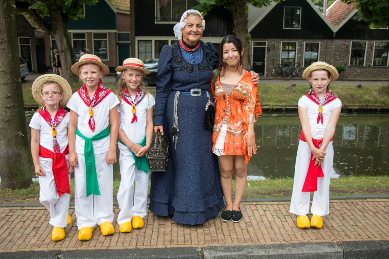 a woman in long dress and five children are standing near water