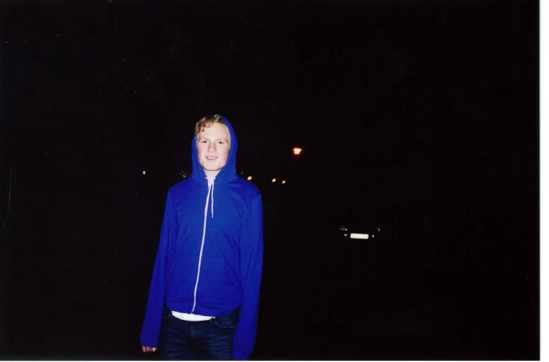 a girl wearing a hoodie is standing outdoors in the dark