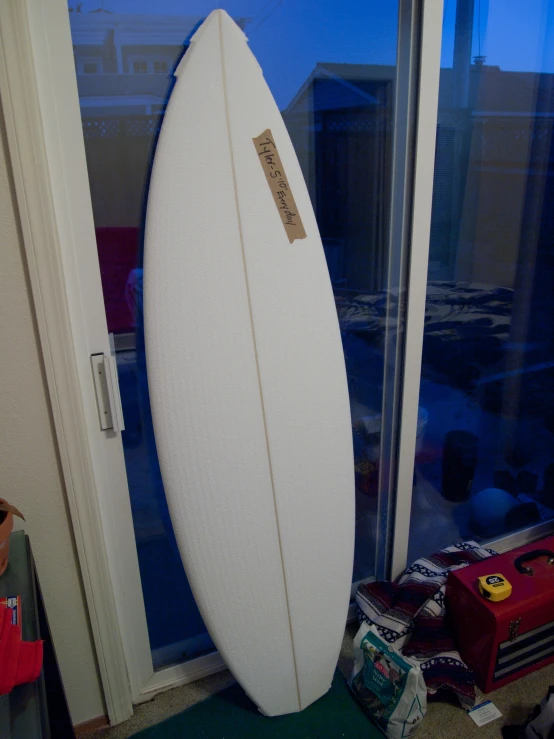 a white surfboard is leaning against a window