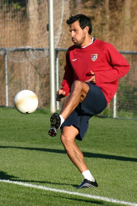 man in red shirt and shorts kicking soccer ball